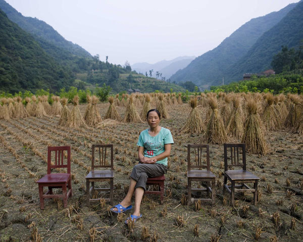 Chen Songying, with four chairs reserved for her husband and three children who left home to work, sits in her farmland in front of her home in a village of Shizhuan town, Shikang city, Northwest China's Shaanxi province, August, 29, 2011.