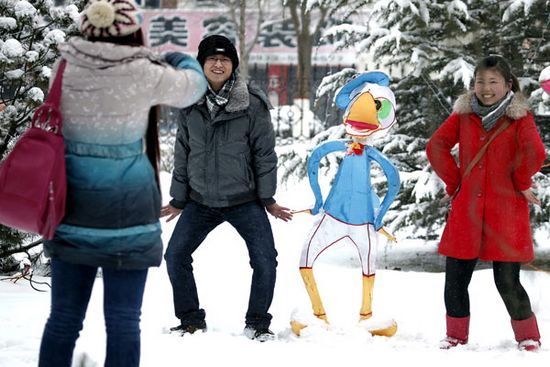 Young people pose next to a cartoon statue in Liuhu Park in Pingliang, Gansu province, on Friday after snow fell on the city. (Photo: China Daily/Yang Xin) 