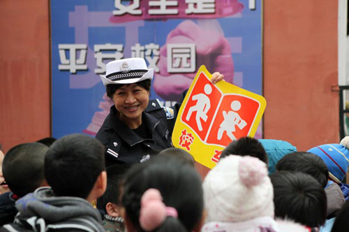 Zhang Ying, a traffic police officer in Shenyang, Liaoning province, shows the sign of the school bus to students at the No 9 primary school in the city's Nanjing Street on March 5. Zhao Jingdong / for China Daily 