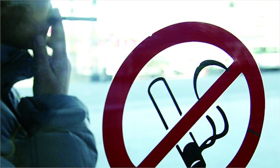 A man smokes near a no-smoking sign at Beijing Junefield Department Stores, Xicheng district.