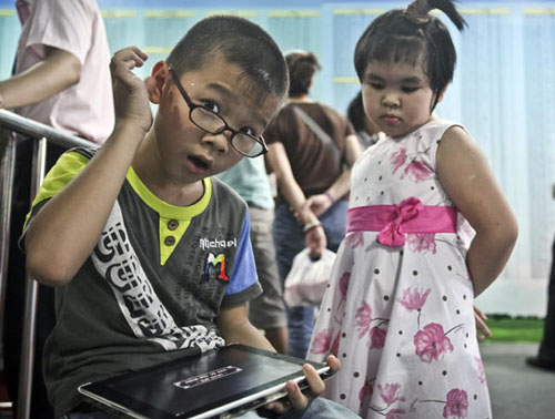 A boy plays with a tablet while waiting for his parents at a sales office in Guangzhou, South China's Guangdong province. Provided to China Daily