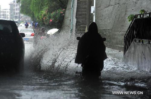 A resident rides in the rain in Wuhan, capital of central China's Hubei Province, June 27, 2012. The local government has initiated level-4 emergency response and sent special work teams to gauge the damage of the rainstorm which started Tuesday afternoon