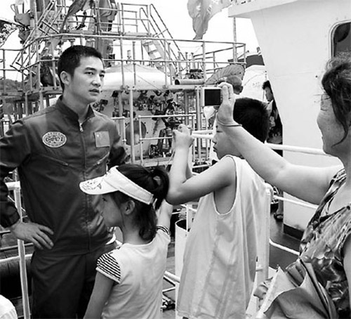 Oceanaut Fu Wentao, one of 11 people in the world who has dived to a depth of more than 7,000 meters under the sea, talks with visitors on Thursday on Xiangyanghong 09, the support ship of China's manned submersible, Jiaolong, in Qingdao, Shandong province. (Li Ziheng / Xinhua)