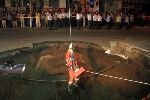 A firefighter in Harbin, capital of Northeast China's Heilongjiang province, goes down into a sinkhole to rescue people who fell into it after the pavement collapsed on Tuesday. Two people were killed and two were injured. Xiao Jinbiao / for China Daily
