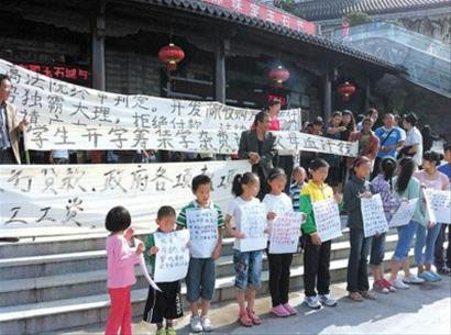 Thirteen children hold signs and ask for their parents' money back outside Guang Xia, a construction company in Dali, south China's Yunnan province on Tuesday, August 14, 2012. [Photo: Agencies]