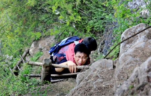 A teachers uses iron ladders to help the students climb over a steep mountain to reach a bridge that they need to cross to get to their school.[Yuan Xiaozhen/gmw.cn]