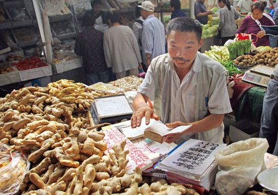 Yao Qizhong sells ginger at a market in Beijing while writing his diary. (Photo: China Daily)