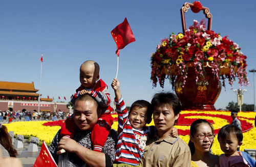 Visitors wave national flags in front of a bed of flowers at the Tian'anmen Square in Beijing on Sept 30. Zhu Xingxin / China Daily