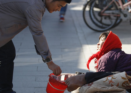 A resident gives cash to a beggar in downtown Beijing on Wednesday. China promised more funds and favorable policies for poverty-stricken populations on Wednesday, which marked the International Day for the Eradication of Poverty. Zhu Xingxin / China Daily