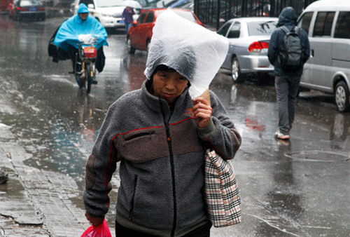 A pedestrian in Beijing uses a plastic bag to shelter herself from rain on Sunday, when a cold front brought rain and chillier temperatures to the city. Zhang Hao/China News Service
