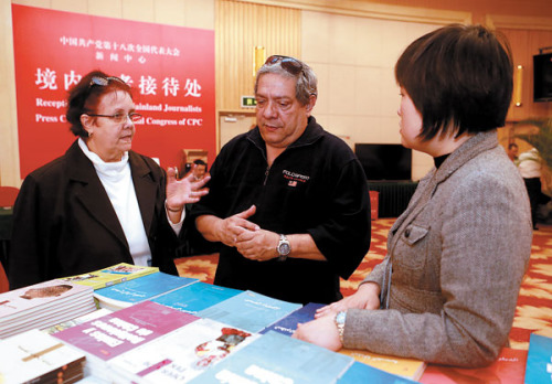 Two reporters from Cuba select free books at the media center for the 18th National Congress of the Communist Party of China on Thursday. [Photo/China Daily]