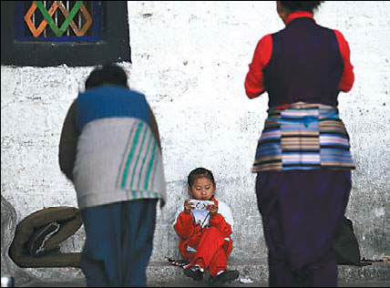 A girl plays a game on her PlayStation Portable console while her family members are praying outside the Jokhang Temple, Lhasa, on Sept 28. Cui Meng / China Daily