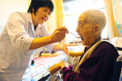An elderly man eats his meal with the help of a caregiver at a nursing home in Jinan, capital of Shandong province. LUO BO / FOR CHINA DAILY