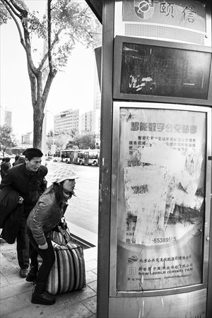 Passengers wait at Dabeiyao bus stop, near Guomao in Chaoyang district on Monday. An LED electronic screen above the billboard, which has never worked, is covered with scratches and graffiti. Photo: Li Hao/GT
