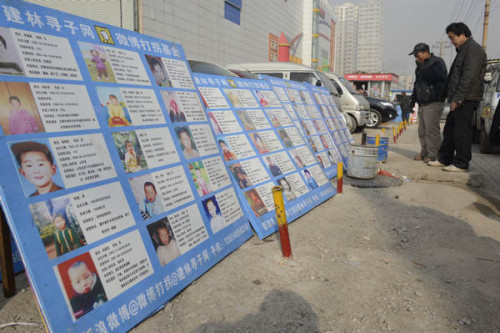 Two pedestrians look at the show board of mission children in Taiyuan, North China's Shanxi province on Nov 18, 2012. [Photo/Asianewsphoto]
