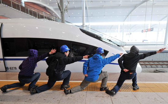 Passengers imitate the hand signals of flight deck crew of aircraft carrier beside a high-speed train at the Harbin West Railway Station in Harbin, capital of Northeast China's Heilongjiang Province, Dec 1, 2012. [Photo/Xinhua]