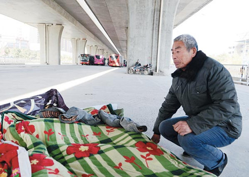 Zhu Yunyou, a migrant worker, unfolds a quilt under an overpass where he lives in Zhengzhou, Henan province, on Monday.[Xiang Mingchao / China Daily]
