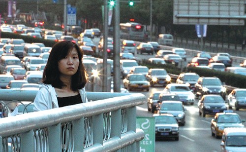 A woman stands on a pedestrian bridge overlooking the Fourth Ring Road in northeast Beijing during rush hour in September. [Photo by Wang Jing / China Daily]