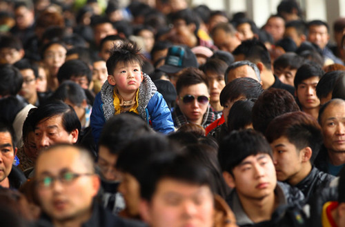 A young boy seems far from impressed as passengers wait to enter Beijing Railway Station on Tuesday. Even bigger crowds are expected over the next few days, as the Spring Festival travel rush gets into full swing. [ZOU HONG / CHINA DAILY]