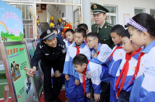 A police offi cer and an offi cer from a local fire brigade teach students at a primary school in Tianjin how to escape a fire. [WU DI / FOR CHINA DAILY]