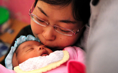 A woman with amyotrophic lateral sclerosis holds her 1-moth-oldd child. The prevalence of ALS wihcih is characterized by motor neuron degeneration, is there in 50,000. [Photo/Xinhua]
