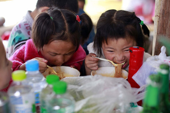 Young survivors get a warm meal at a rescue center in Longmen township, Lushan, on Sunday. [Feng Yongbin/China Daily]