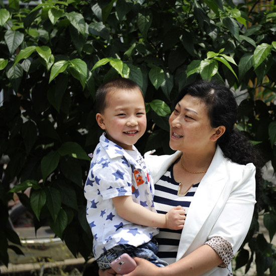 Hu Yanhui and her son before their house in Beichuan county, Sichuan province on May 3, 2013. Hu, 37, gave birth to her son Fan Zihe on Autumn 5, 2009. She lost her only 8-year-old daughter in the 2008 earthquake. She and her families were resettled into a new house over 120 square meters by the local government in June 2011. [Pan Songgang and Duan Xuemei/Asianewsphoto]