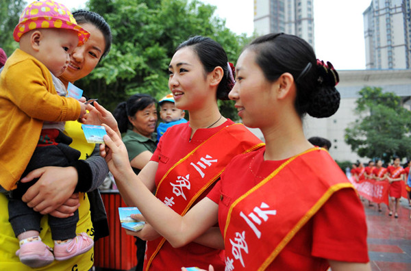 Chen Xiaoxue (middle), the champion of Miss Tourism International 2012, accompanies a female coach attendant, and communicates with a local citizen about passenger rail transportation on June 18, 2013 at Dong Fanghong square in Lanzhou city. [Photo / Xinhua]