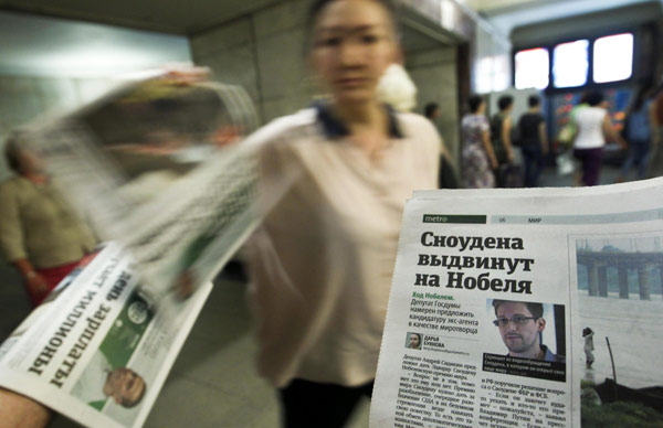 An employee distributes newspapers, with a photograph (R) of former US spy agency contractor Edward Snowden seen on a page, at an underground walkway in central Moscow July 2, 2013.[Photo/Agencies]