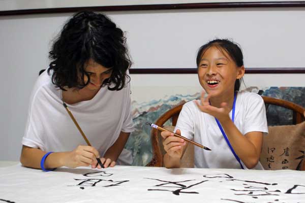 Wei Lai (right), 11, teaches 15-year-old Michela Orsi from Italy how to use a Chinese calligraphy brush on Sunday in Beijing. Orsi is one of 117 middle school students from 10 countries participating in the You and Me, in Beijing BFSU Summer Camp 2013. The camp, organized by Beijing Foreign Studies University and the Confucius Institute Headquarters, aims to create the cultural exchanges between China and other countries. [Zou Hong/China Daily]
