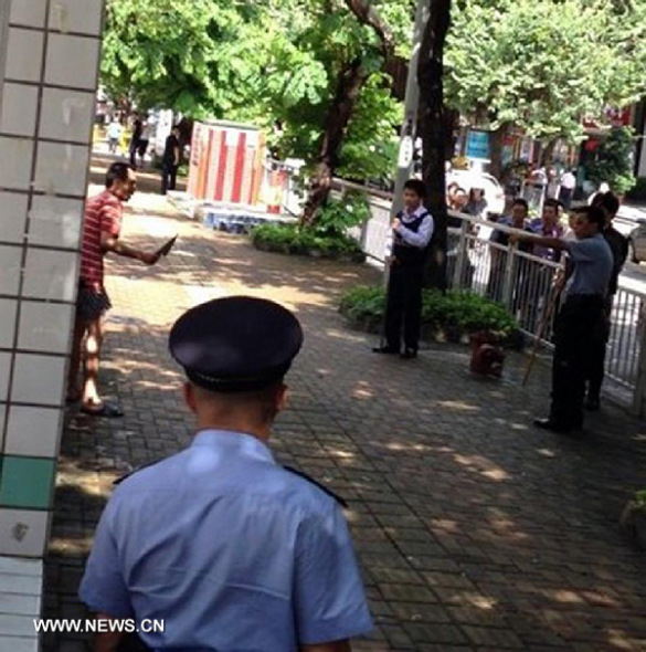 Photo taken on July 29, 2013 by mobile phone shows policemen confronting a man holding a knife in Luohu District of Shenzhen City, south China's Guangdong Province. Three people died and another five were injured in a knife attack that occurred Monday in the city of Shenzhen. Police received a call at 9:45 a.m. Monday saying that a man was randomly attacking passersby with a knife on the side of a road in the city's Luohu District. Police later detained the man and rushed the injured to the hospital. The man, surnamed He, was also sent to the hospital for treatment, as he injured himself during the attack. Initial investigation showed that the man had a history of mental illness. (Xinhua) 