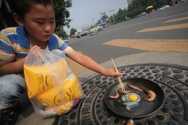 A boy cooks an egg and shrimp on a manhole cover in a road in Jinan, Shandong province, on Wednesday. Many cities around China are suffering sweltering heat, and experts say the situation will continue until mid-August. Zheng Tao / for China Daily