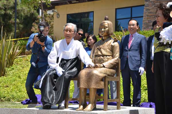 Kim Bok-dong, a victim of the Japanese military during World War II, sits in the empty chair of the comfort women memorial during the unveiling ceremony in Glendale, California on Tuesday. The statue is a tribute to Asian comfort women who were forced into sexual slavery by Japanese troops. [Liu Yiyi / China Daily]