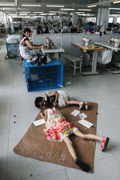 Migrant workers' children play on the ground as their parents work nearby at a plant in Jiashan county, Zhejiang province, July 17. [Photo by Hu Lingxiang/Asianewsphoto]