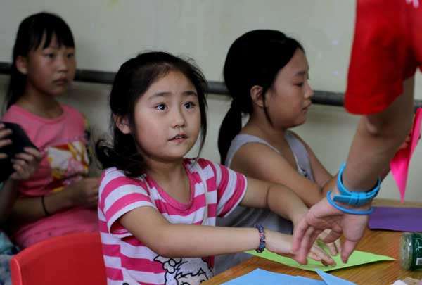 Migrant children play paper-folding games at the Mulan Activity Center in the Changping district of Beijing on Aug 7. The center has a library and organizes games. Xu Huiyan / for China Daily
