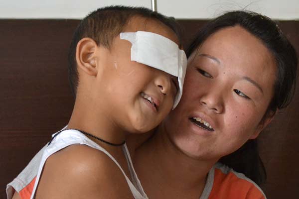 In his mother's arms, 6-year-old Guo Bin, whose eyes were gouged out by a woman last week, thanks a man who donated money to him in a hospital in Taiyuan,Shanxi province, on Tuesday. Police identified the boy's aunt, who has committed suicide, as the suspect, though doubts remain. [Hou Liqiang / China Daily]