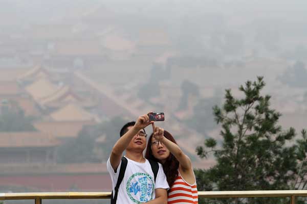 A couple in Beijing's Jingshan Park take photos against the background of a smog-shrouded Forbidden City as bad air pollution hit the capital on June 30. ZHUO ENSEN / FOR CHINA DAILY