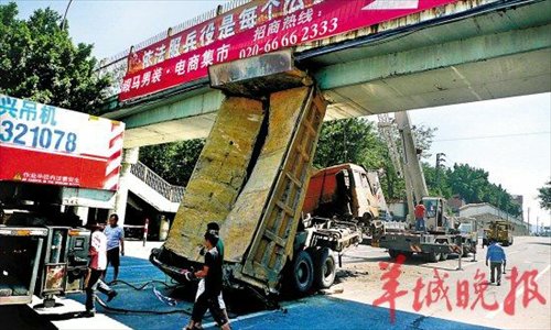 Two cranes work to remove the dump truck from under a pedestrian bridge in Guangdong Province on Thursday. Witnesses say the driver raised the bed in order to stop the truck after a brake failure. Photo: Yangcheng Evening News