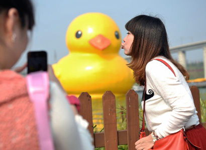 A visitor poses for a photo with a giant rubber duck on the Yuanbo Lake in the Garden Expo Park in Beijing, capital of China, Sept. 6, 2013. The 18-meter-tall inflatable rubber duck, created by Dutch artist Florentijn Hofman, is expected to visit Beijing from September to October. (Xinhua/Li Xin)