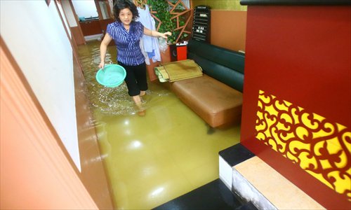 A shop owner grabs a basin to bail floodwater out of her shop on Lishan Road in Putuo district Tuesday. The heavy rain flooded the stores on the road, forcing some shopkeepers to borrow water pumps to remove the floodwater. Photo: Cai Xianmin/GT