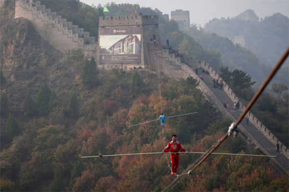 Uygur tightrope walker Adili Wuxor (in red) and his apprentice, Yakup Jang, walk on a 331-meter rope spanning two towers of the Great Wall at Huangyaguan Pass in Jixian, a county in Tianjin, on Friday. PHOTOS BY KUANG LINHUA / CHINA DAILY