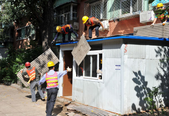 Urban patrol officers, known as chengguan, organize the demolition of illegal buildings in a Beijing community on Sept 10. Pu Dongfeng / for China Daily
