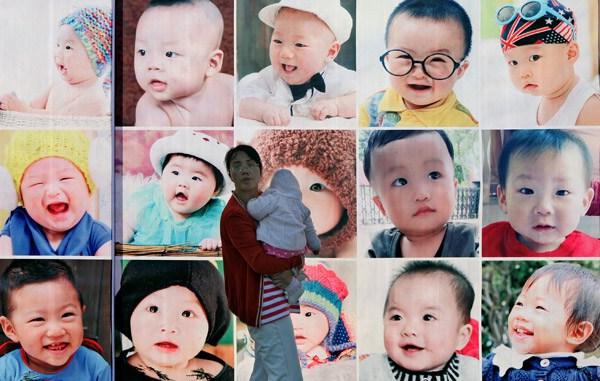 A mother holds her child in front of a wall with photos of babies in Taizhou, Zhejiang province, on Sunday. Couples will be allowed to have two children if one of the parents is an only-child. Pan Kanjun / For China Daily