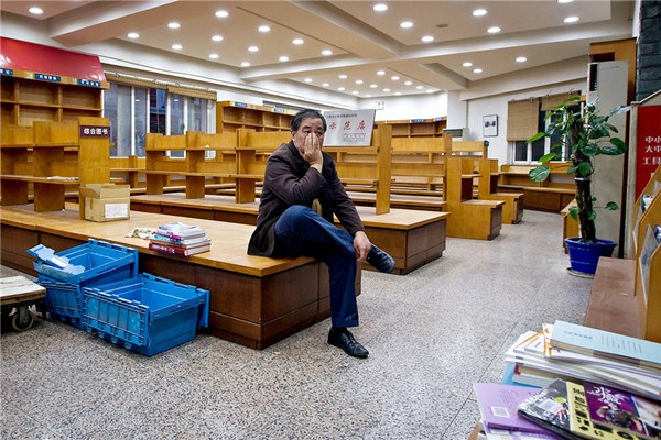 A staff member surnamed Chen sits on an empty book stand Tuesday at a Xinhua Bookstore outlet on Sichuan Road N. Chen worked for more than 30 years at the store, which closed on Monday due to continuing losses. The store had a history of more than 90 years. Many brick-andmortar bookstores have closed in the city due to the impact of online bookstores offering a wider choice, easy delivery and discounts, plus the move toward digital books. (Kou Cong) 
