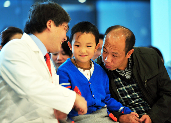 Dennis Lam Shun-chiu (left), an eye doctor from Hong Kong, sends his best wishes to 6-year-old Guo Bin on Thursday, as he left Lam's hospital in Shenzhen after surgery to implant cosmetic eyes. The boys' eyes were gouged out by his aunt in August. Chen Jimin / China News Service