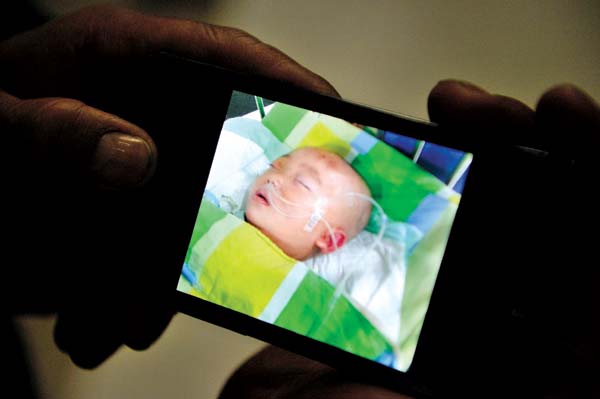 Xinyuan's grandfather displays a photo of the 18-month-old boy receiving treatment in the ICU. Li Jian / Xinhua 