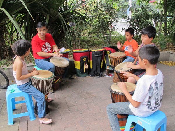 Zeng Liming leads his students in a drum circle in a square by Shenzhen's Nanshan Book City. Zeng is teaching children how to play the African hand drum known as the djembe. Chen Wenli / for China Daily