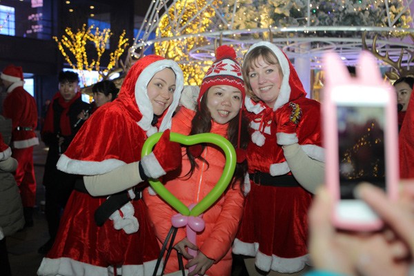A Beijing resident poses with foreign performers in the city's Sanlitun shopping district to celebrate Christmas Eve on Tuesday. Photo by Wang Jing / China Daily
