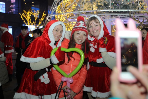 A Beijing resident poses with foreign performers in the city's Sanlitun shopping district to celebrate Christmas Eve on Tuesday. Photo by Wang Jing / China Daily
