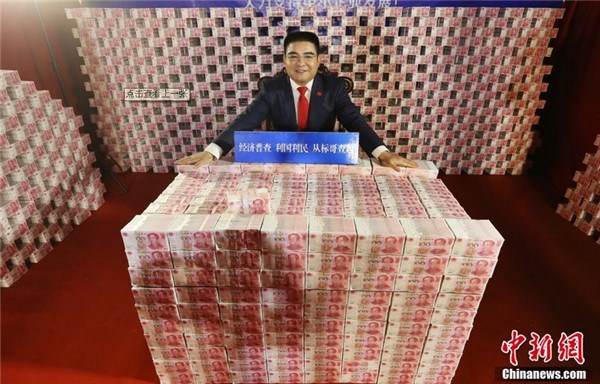Chen Guangbiao, a Chinese entrepreneur and philanthropist, takes a picture in a studio with stacks of RMB bills to promote the upcoming national economic census in Nanjing, capital of East China's Jiangsu province, on Dec 24, 2013. [Photo/Chinanews.com]